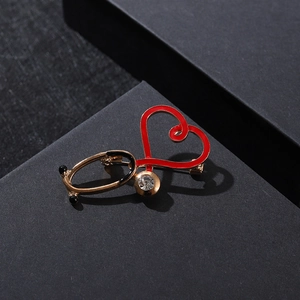 Detail of stethoscope heart brooch with red enamel and a white zircon on black box