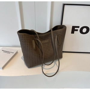 Detailed view of deep brown woven tote bag with slim dual straps and leather logo tag