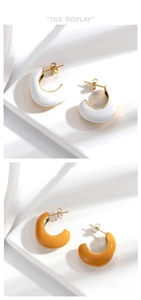 Detail of minimalist C-shaped enamel earrings in white and ginger yellow over gold metal