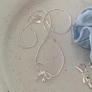Elegant 925 sterling silver bow pendant necklace on a textured ceramic display plate