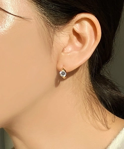 Close-up of minimalist gold earring with a round-cut zircon on female ear lobe