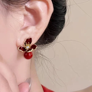 Elegant gold flower earrings with red enamel petals and zircon center on model