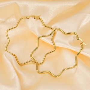 Detailed close-up of gold geometric star hoop earrings on a luxury satin silk background