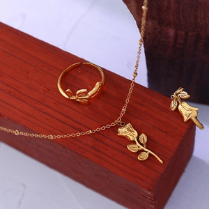 Elegant gold rose flower necklace and adjustable ring set on a red textured base