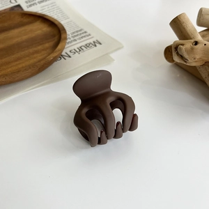 Detailed view of a dark brown matte hair claw clip on a minimalist wooden tray display