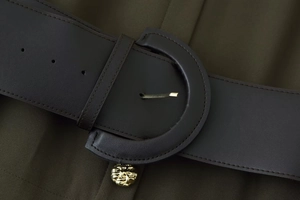 Detail of dark brown faux leather wide belt with gold D-ring buckle on green midi dress