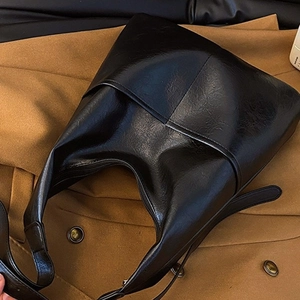 Sac fourre-tout en cuir noir brillant au design minimaliste posé sur un vêtement beige