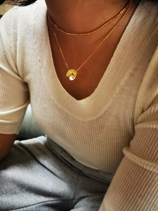 Detail of layered gold brass necklaces with abstract petal pendant on a knit sweater