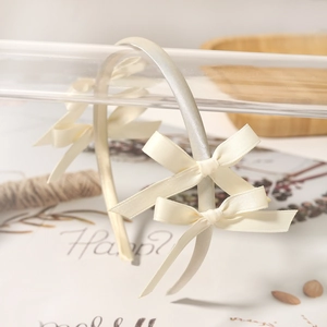 Detail of a creamy white satin headband featuring delicate bows in a soft aesthetic style