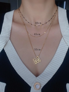 Detailed view of layered 18k gold-plated necklaces with M pendant on a model