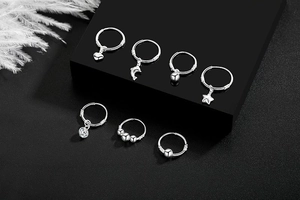 Detailed set of seven silver hoop earrings with diverse charms on black geometric display