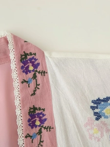 Dettaglio del tessuto in cotone rosa con ricamo a punto croce e colletto in pizzo fine