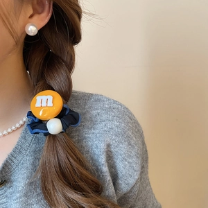 Détail d'un chouchou en tissu avec perles et breloque orange lettre m en résine