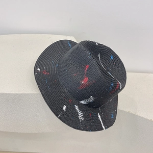 Detailed view of black woven straw hat with artistic red, white and blue paint splatter design