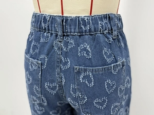 Detail of frayed heart patterns and elastic waistband on dark blue denim straight jeans