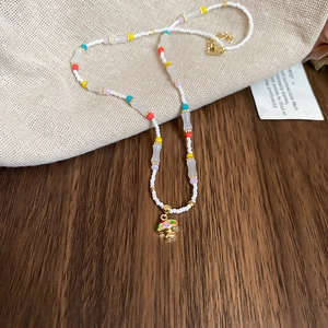 Macro shot of colorful beaded necklace featuring a gold mushroom pendant with enamel dots