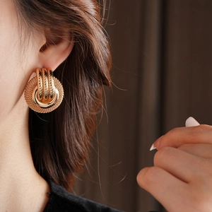 Close-up of a model wearing golden hollow mesh disk earrings with twisted rings