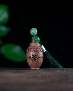 Detailed view of hollow carved sandalwood pendant with green beads and silk tassels