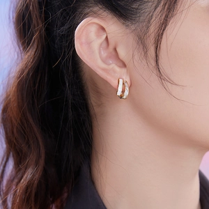 Close-up of double layered gold earrings with white enamel and cubic zirconia on model