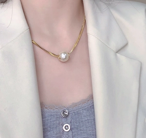 Close-up of elegant double-layered gold snake chain necklace with a large white pearl