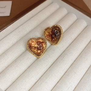 Close-up of amber resin heart earrings with gold trim on a velvet jewelry display tray