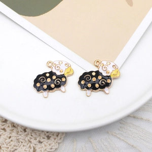 Macro detail of two black and white sheep enamel pendants with golden alloy outlines