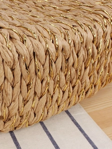 Minimalist straw handbag with woven gold thread texture on a natural wooden background