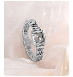 Close-up of a silver square quartz watch with a metal link strap on a soft fabric background