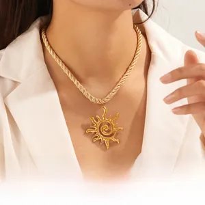 Détail du collier pendentif soleil doré avec chaîne torsadée sur blazer blanc