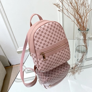 Pink mini backpack with brown floral pattern and adjustable straps on a glass table