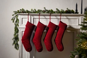 Detail of four red knit Christmas stockings hanging on a white mantel with green pine needles