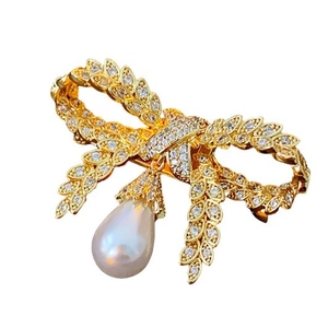 Broche nœud plaquée or avec zircons étincelants et perle goutte sur fond blanc