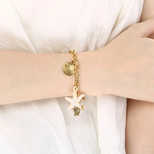 Gros plan d'un bracelet doré 18K avec pendentifs étoile de mer et coquillage sur le poignet