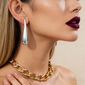 Detail view of silver teardrop earrings on model paired with chunky gold chain necklace