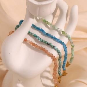 Detail view of colorful natural stone beaded anklets hanging on a white hand model