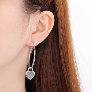 Close-up of a silver heart drop earring with grey enamel inlay worn by a female model