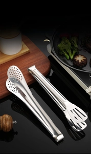 Detail of thickened stainless steel tongs with hollow design on black kitchen surface