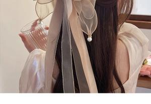 Detail of elegant beige organza bow hair clip with pearl charms on model's head