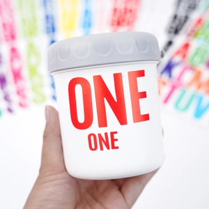 Close-up of a white tumbler with a grey lid featuring bold red ONE letter stickers