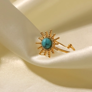Detail shot of sun-shaped gold ring with turquoise inlay on soft beige silk
