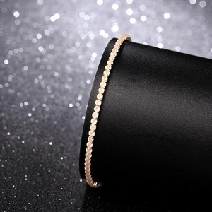 Close-up of a delicate 2mm gold-plated tennis bracelet with shimmering crystals on a stand