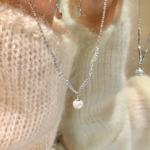 Close-up of elegant silver pearl necklace with zircons worn on a beige knit sweater