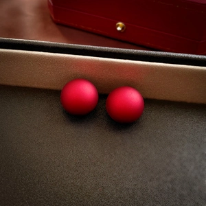 Macro shot of matte dark red bead stud earrings on a luxury leather display tray