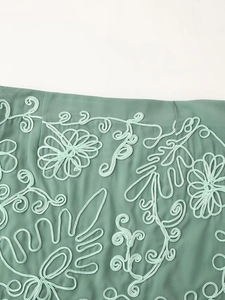 Gros plan sur une robe verte de vacances avec des détails de broderie florale en cordon