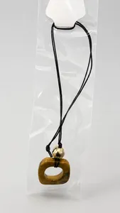Detail of square resin pendant on black cord necklace inside transparent packaging bag