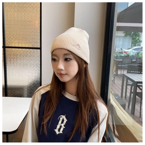 Detailed view of a beige knitted beanie on a female model in a cozy cafe setting.