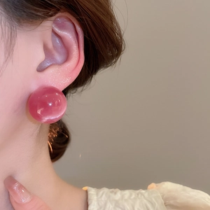 Close-up of a pink round cat eye stud earring worn by a model for a sweet style