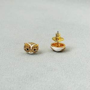 Cute golden owl earrings with white enamel and sparkling crystals on grey background