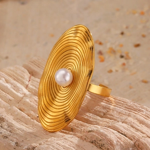Golden oval textured ring with inlaid pearl and concentric rings on a natural wood base