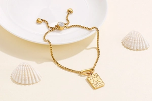 Detail of adjustable gold-tone bracelet with rectangle pendant and engraved celestial charms
